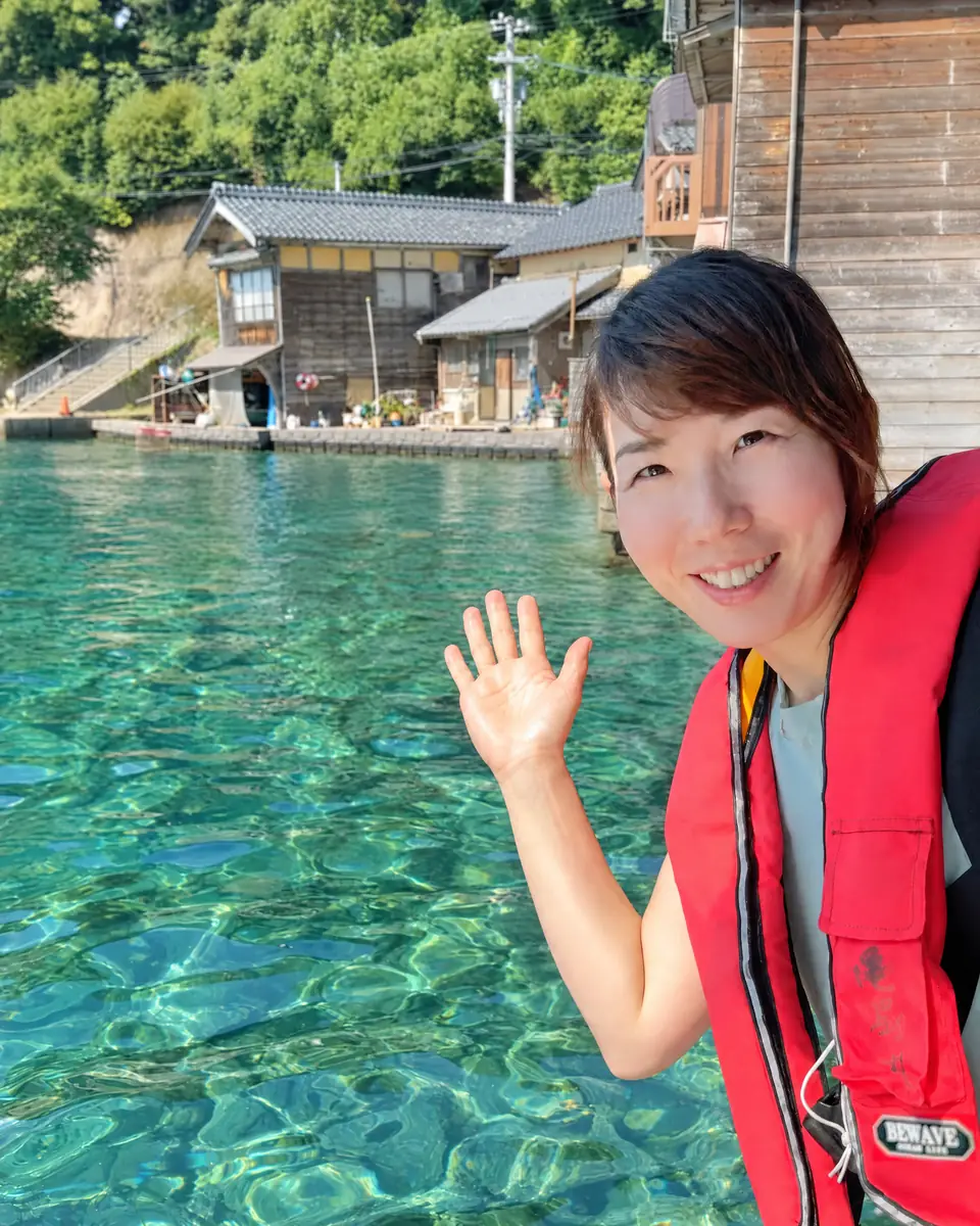 Hiroko waving from a boat in front of the boathouses of Ine