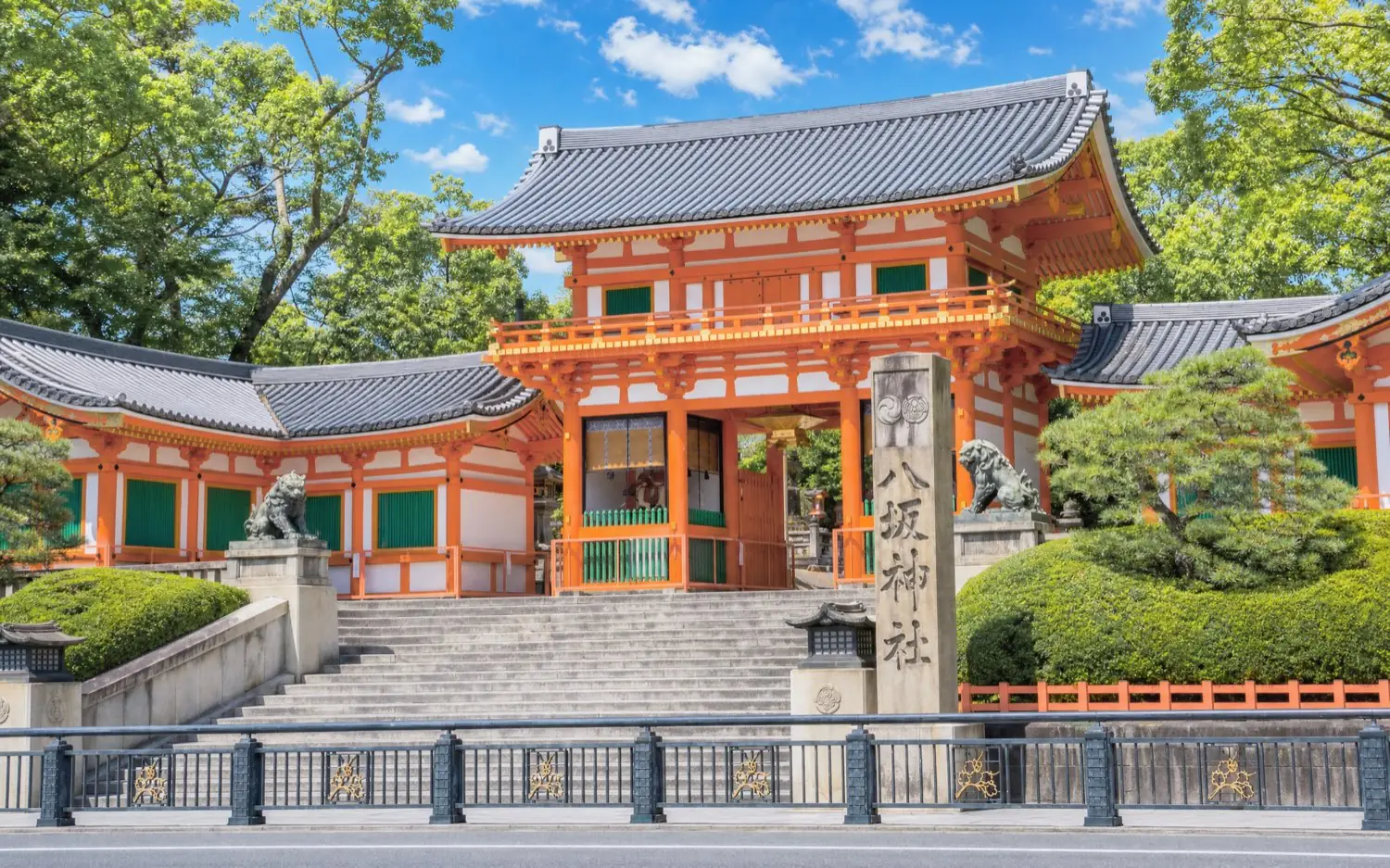 The vermilion west gate of Yasaka Shrine surrounded by fresh green