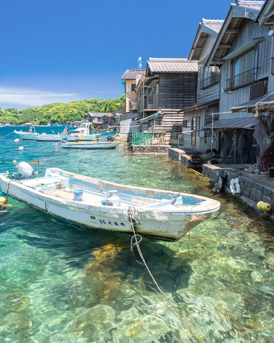 A small boat on the clear water in front of a boathouse