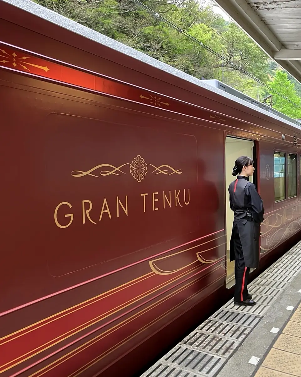 A crew member at the door of the deep-red GRAN Tenku train
