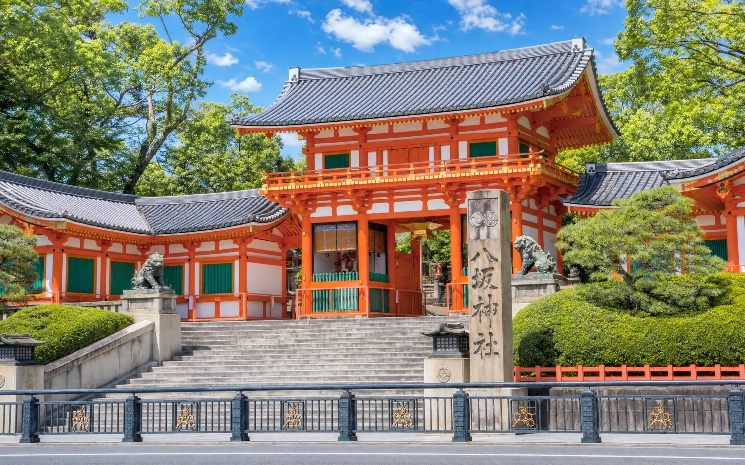 The vermilion west gate of Yasaka Shrine surrounded by fresh green